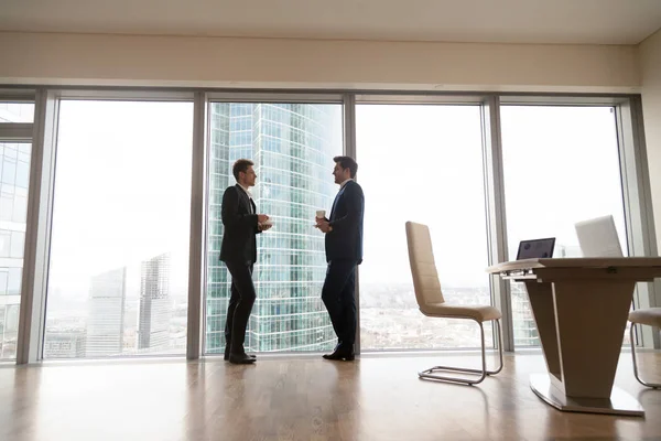 Two businessmen standing at full-length window in office, coffee — Stock Photo, Image