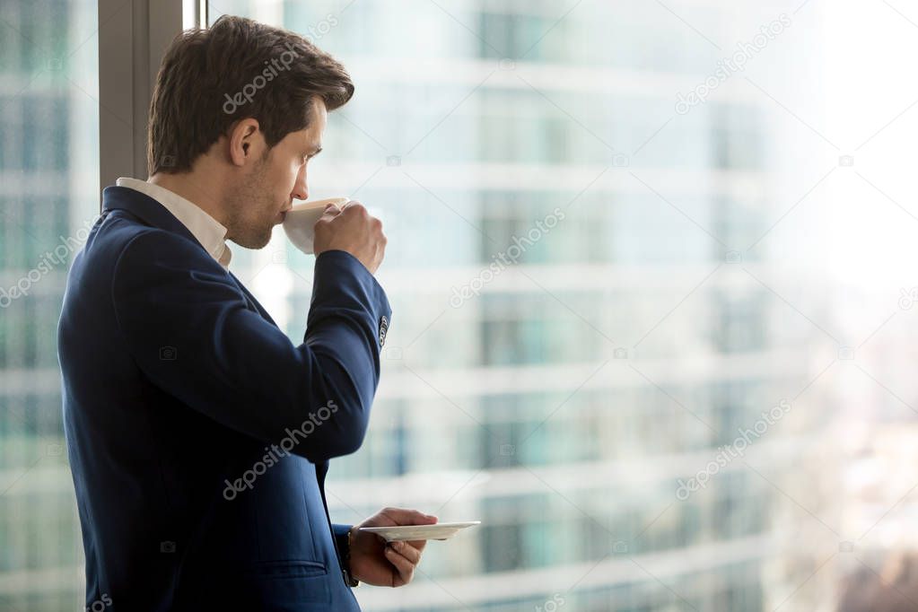 Thoughtful businessman drinking coffee, looking through office w