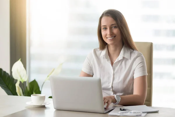 Pen forretningskvinne som jobber med laptop, smiler til kamera på wo – stockfoto