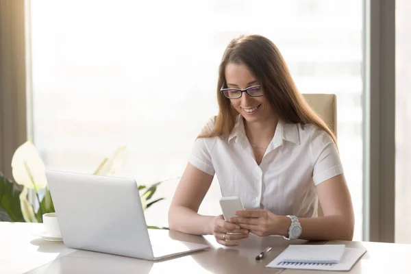 Hermosa dama de negocios sonriente usando teléfono inteligente sentado en offi — Foto de Stock