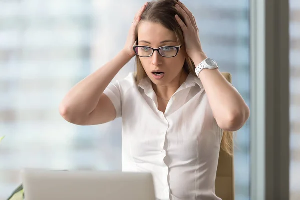 Удивлённая шокированная деловая женщина смотрит на ноутбук, голова в руках — стоковое фото