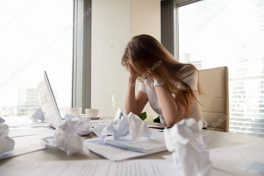 Frustrated businesswoman sitting at desk with crumpled paper, no