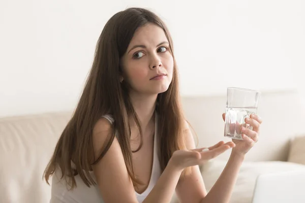 Mulher preocupada duvidosa segurando pílula, vidro de água em casa — Fotografia de Stock
