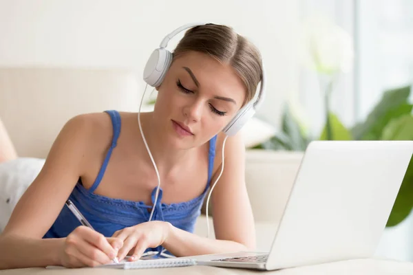 Senhora em fones de ouvido fazendo notas de palestra on-line — Fotografia de Stock