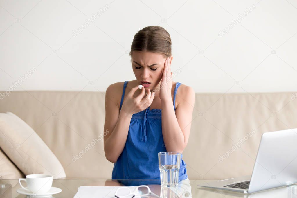 Woman feeling headache and drinking pill at home