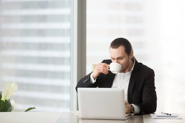 Зайнятий молодий бізнесмен п'є каву під час роботи на ноутбуці . — стокове фото