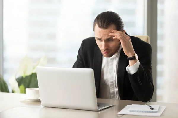 Molesto hombre de negocios confundido mirando la pantalla del ordenador portátil en el lugar de trabajo — Foto de Stock