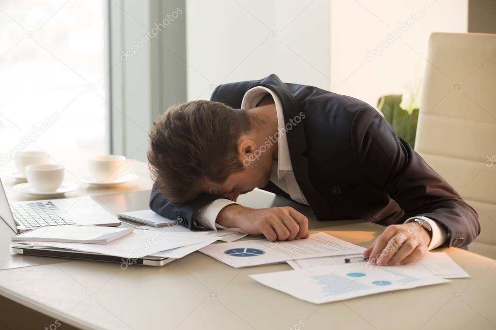 Tired young businessman sleeping on desk in office