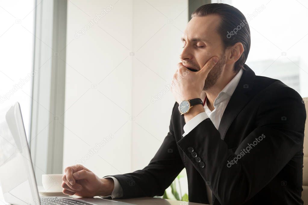 Tired sleepy businessman yawning in front of laptop at workplace