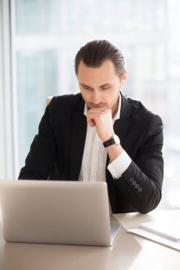 Ofis içinde laptop üzerinde ciddi düşünceli işadamı.