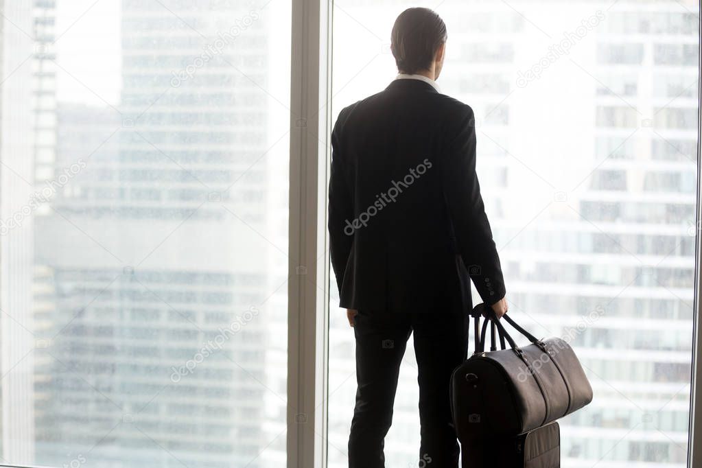 Businessman with luggage standing in front of large window.