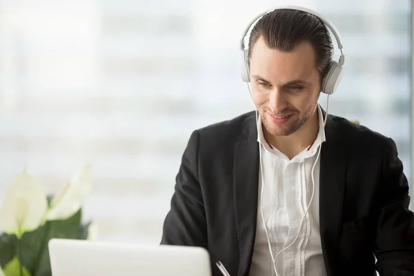 Lächelnder Geschäftsmann mit Kopfhörer blickt auf Laptop-Bildschirm. — Stockfoto