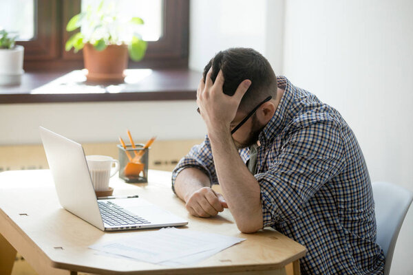 Depressed man looking in his laptop computer receiving bad news.