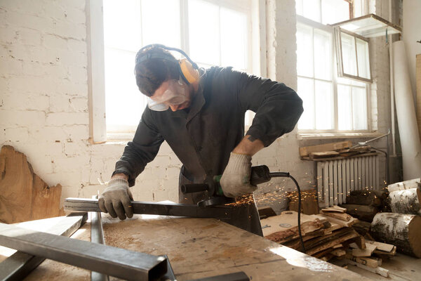 Young workman grinding steel metal profile pipe in workshop inte