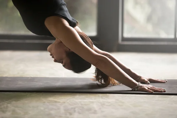 Jonge aantrekkelijke vrouw in adho mukha svanasana poseren, studio terug — Stockfoto