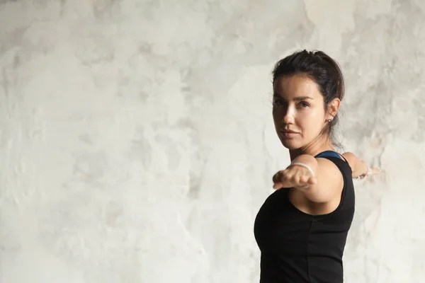 Jovem mulher atraente em Virabhadrasana II pose, parede backgroun — Fotografia de Stock