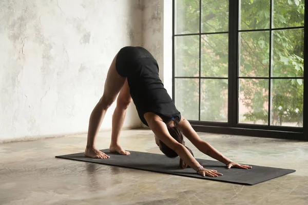 Ung attraktiv kvinna i adho mukha svanasana pose, studio tillbaka — Stockfoto