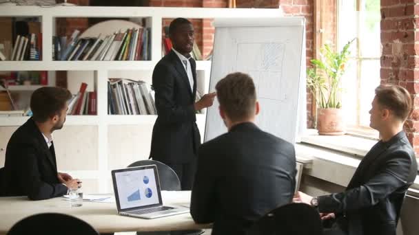 Hombre de negocios afroamericano dando presentación a socios masculinos caucásicos con rotafolio — Vídeos de Stock