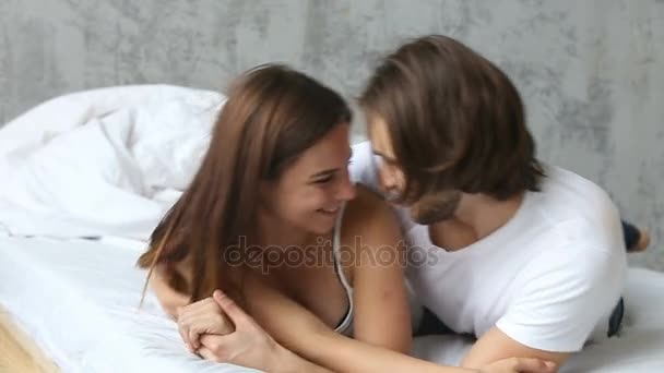 Young happy couple smiling embracing having fun lying on bed — Stock Video