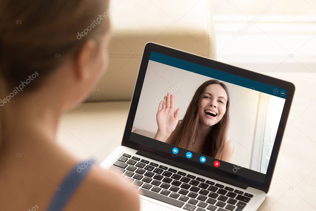 Happy young girl waving to girlfriend from laptop screen.