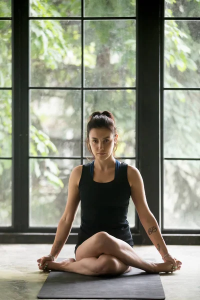 Young attractive woman in Gomukasana pose, studio background