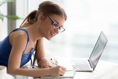 Gülümseyen genç kadın çevrimiçi eğitim dizüstü bilgisayar, notlar, sel