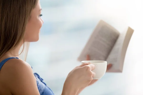 Молодая женщина читает книгу, держит чашку кофе, закрывается — стоковое фото