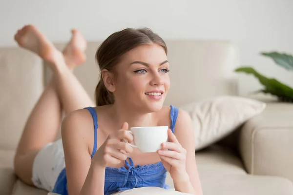 Mulher sonhadora relaxando no sofá confortável, desfrutando de xícara de café — Fotografia de Stock