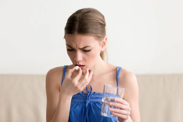 Worried sick woman holding pill, glass of water at home — Stock Photo, Image