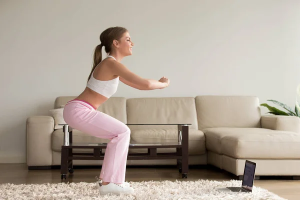 Joven mujer deportiva haciendo ejercicios en cuclillas en casa, en línea trainin — Foto de Stock