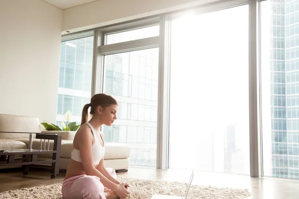 Mujer joven estirándose, haciendo ejercicio de yoga con laptop en casa — Foto de Stock
