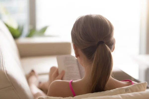 La vista trasera a la mujer que lee el libro en el sofá en casa — Foto de Stock