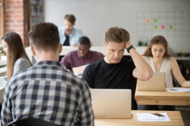 Workplac dizüstü bilgisayar ekranına bakarak çapraşık genç işadamı