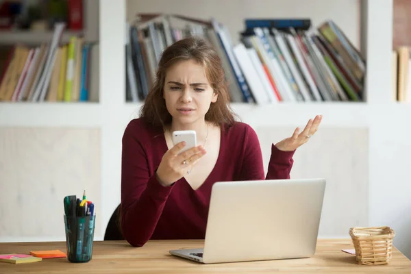 Frustrated female entrepreneur looking at cellphone and shruggin — Stock Photo, Image