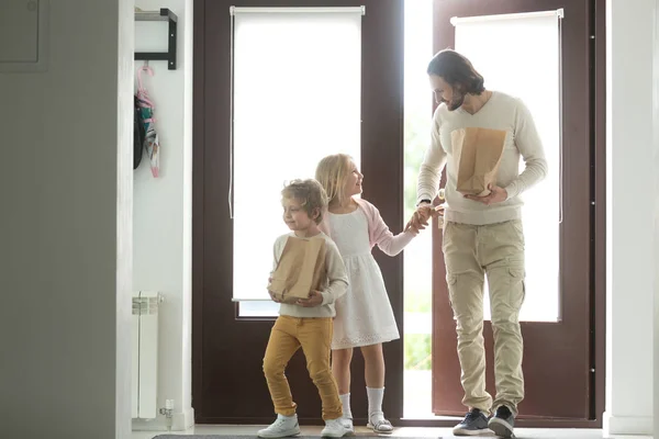 Père souriant avec des enfants rentrant à la maison tenant des sacs en papier — Photo