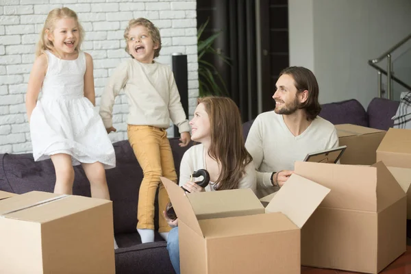 Family with kids playing unpacking boxes, moving in new home