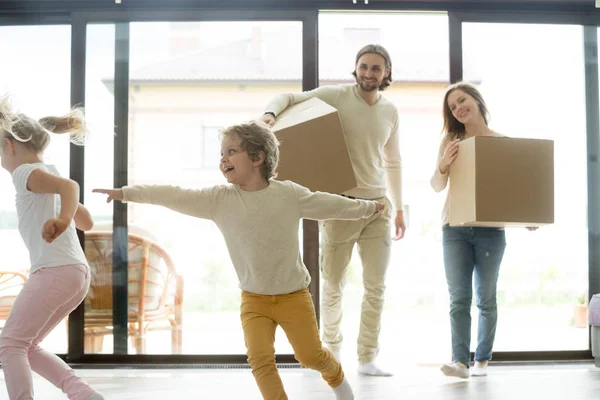 Niños jugando en casa nueva, padres sosteniendo cajas, día de mudanza — Foto de Stock