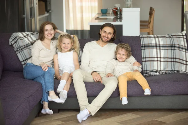 Happy family of four sitting on sofa looking at camera — Stock Photo, Image