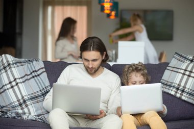 Father and son using laptops sitting on sofa at home clipart