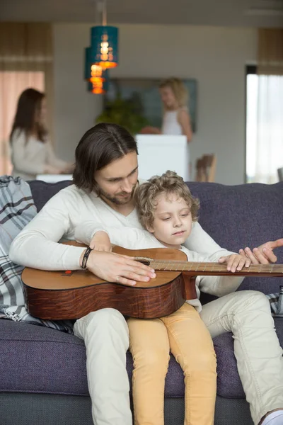 Тато навчає маленького сина грати на гітарі, дочка готує допомогу мо — стокове фото
