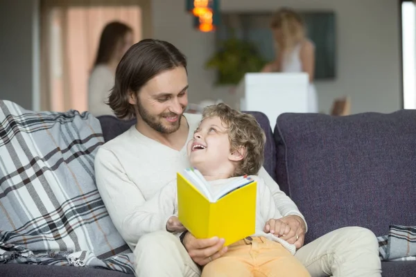 Батько і син читають книгу, сидячи на дивані вдома — стокове фото