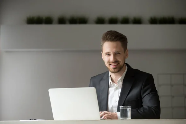 Sorridente giovane uomo d'affari in giacca e cravatta con computer portatile guardando la fotocamera — Foto Stock