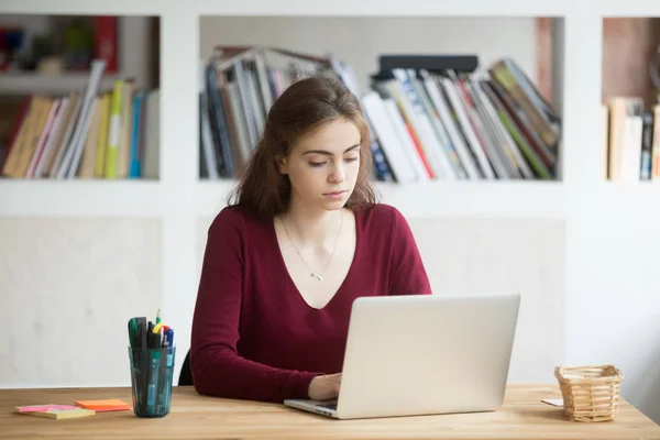 Mladí zaměřený ženský student pracuje na notebooku sedí u stolu — Stock fotografie