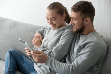 Tablet birlikte evde kanepede kullanma çift kucaklayan gülümseyen