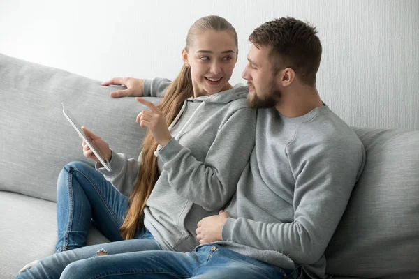 Joven pareja feliz hablando sentado en el sofá usando tableta digital — Foto de Stock