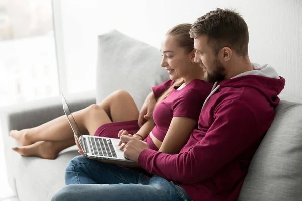 Glada unga paret sitter på soffan med laptop dator togethe — Stockfoto