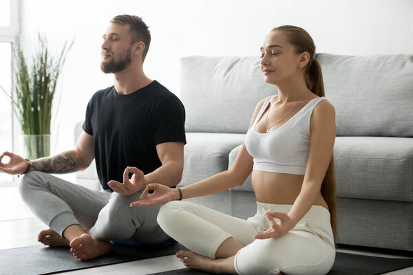 Young couple meditating together doing yoga at home on mat