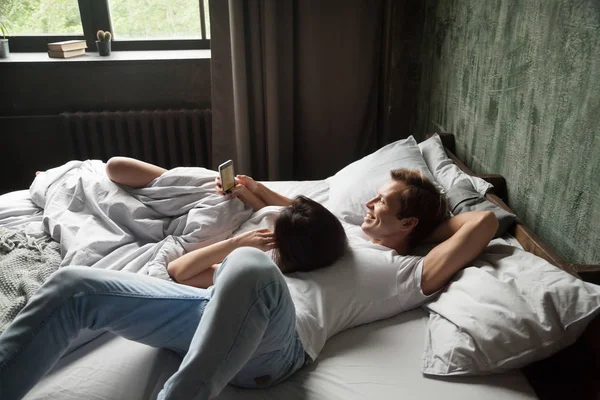 Young couple using mobile phone apps relaxing on bed together — Stock Photo, Image