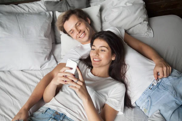 Leende attraktiva tusenåriga par använda smartphone liggande i b — Stockfoto