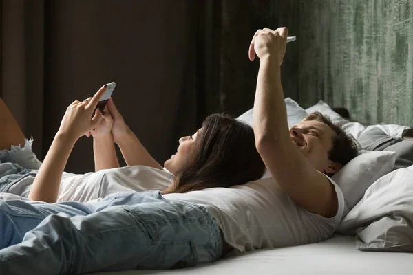 Concepto de adicción móvil, pareja joven usando teléfonos inteligentes mintiendo o — Foto de Stock